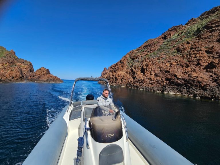 Intérieur d'un bateau avec un homme pilotant, des parois rocheuses en arrière-plan.
